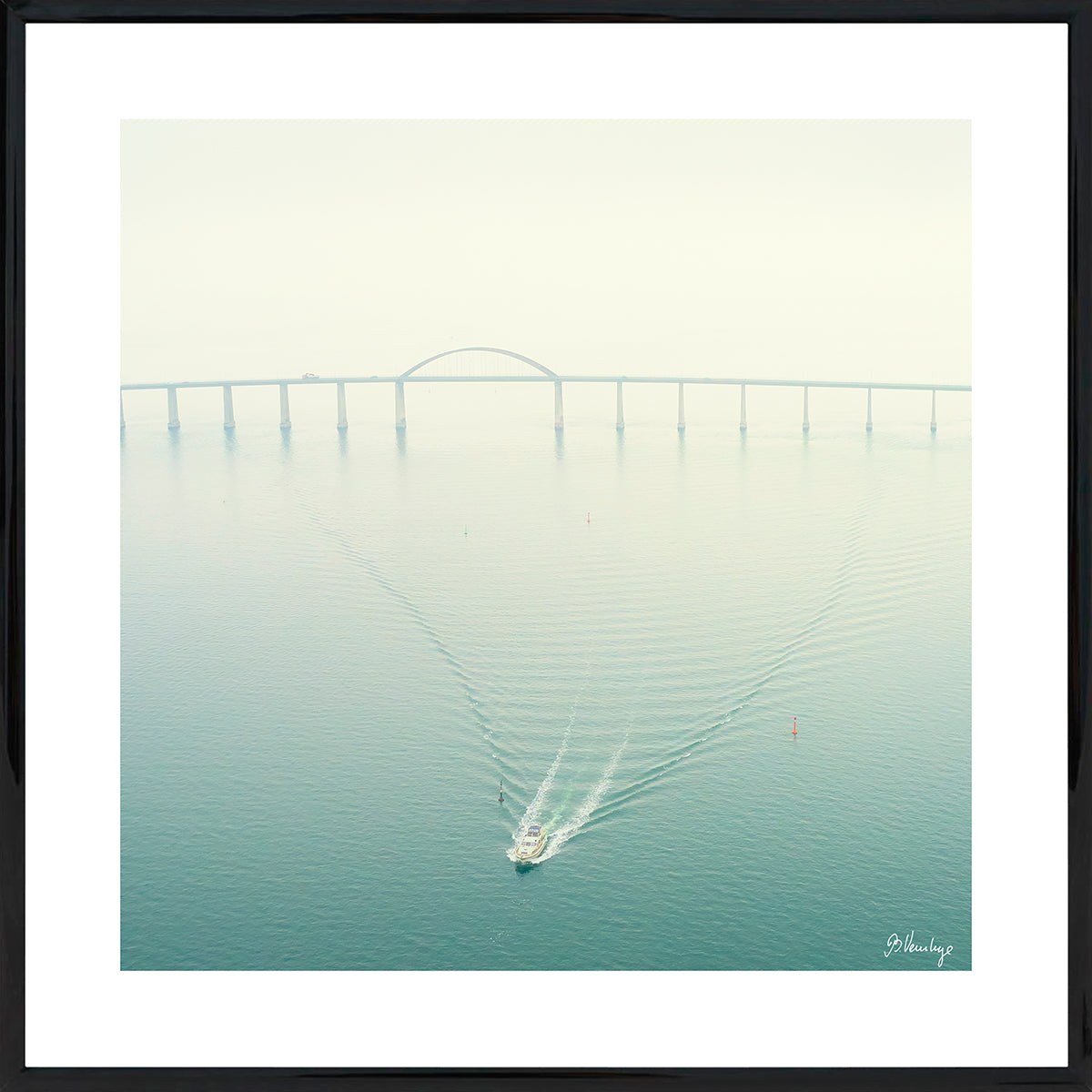 Langelandsbroen på en diset dag. En mindre båd trækker mønstre i vandet. Sart tyrkisgrøn med en rød bøje.